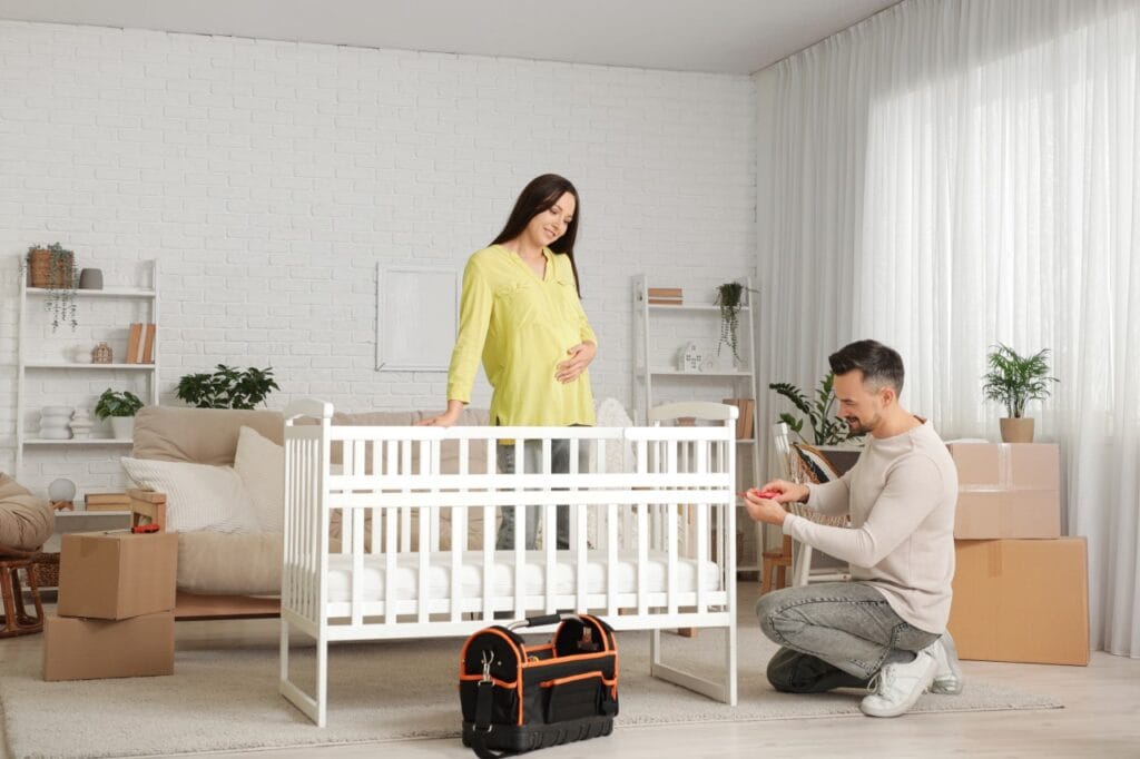 montaj pătuț de lemn în camera copilului, cuplu pregătește mobilier pentru nou-născut acasă