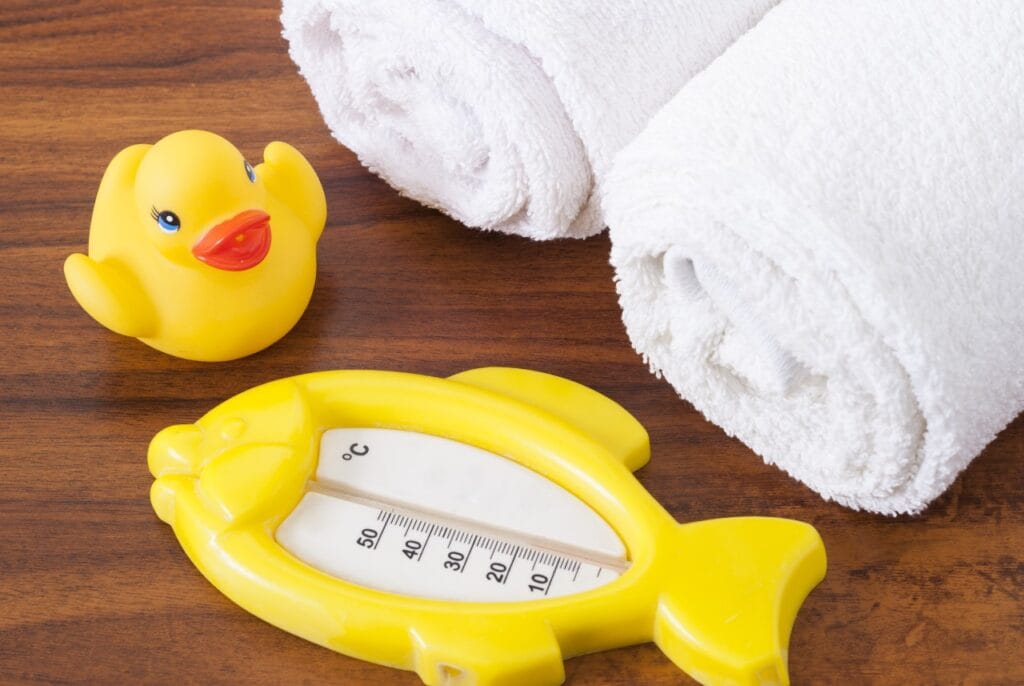termometru de baie în formă de pește galben și jucărie rață pe prosop alb, accesorii sigure pentru copii