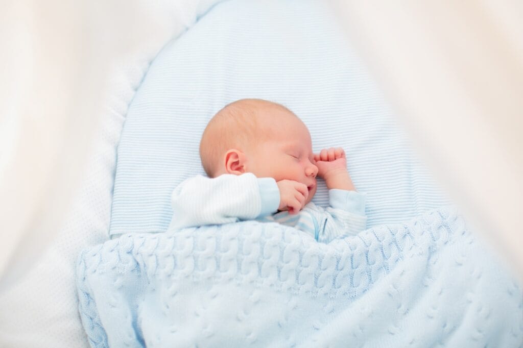 bebeluș dormind liniștit în pătuț cu lenjerie albastră cu design pastel, imprimeuri delicate