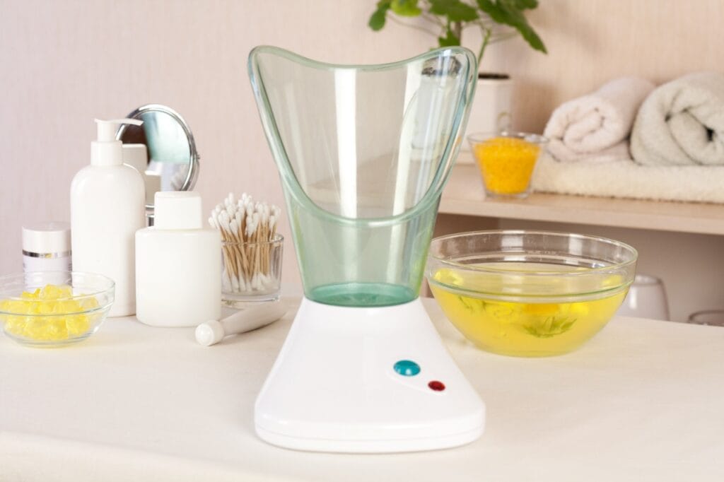 Ritual complet de îngrijire cu saună facială acasă sauna facială pe masă în decor de baie, alături de produse de îngrijire și accesorii pentru ten