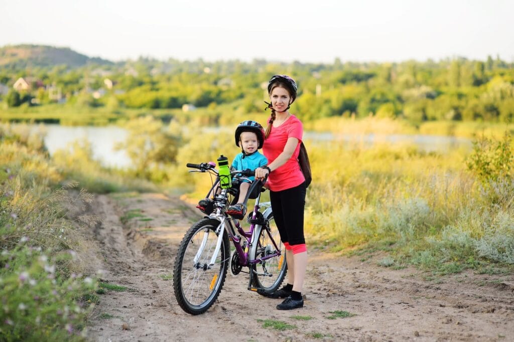 Plimbare cu bicicleta: copil fericit și părinte relaxat Mamă și copil în plimbare cu bicicleta pe drum lung, amândoi poartă cască și zâmbesc, confort și siguranță la drum.