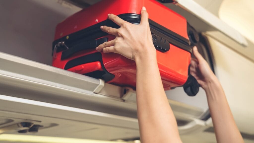 Cum arată un troler cu sistem TSA în compartimentul avionului troler de cabină roșu cu sistem TSA introdus în compartimentul avionului