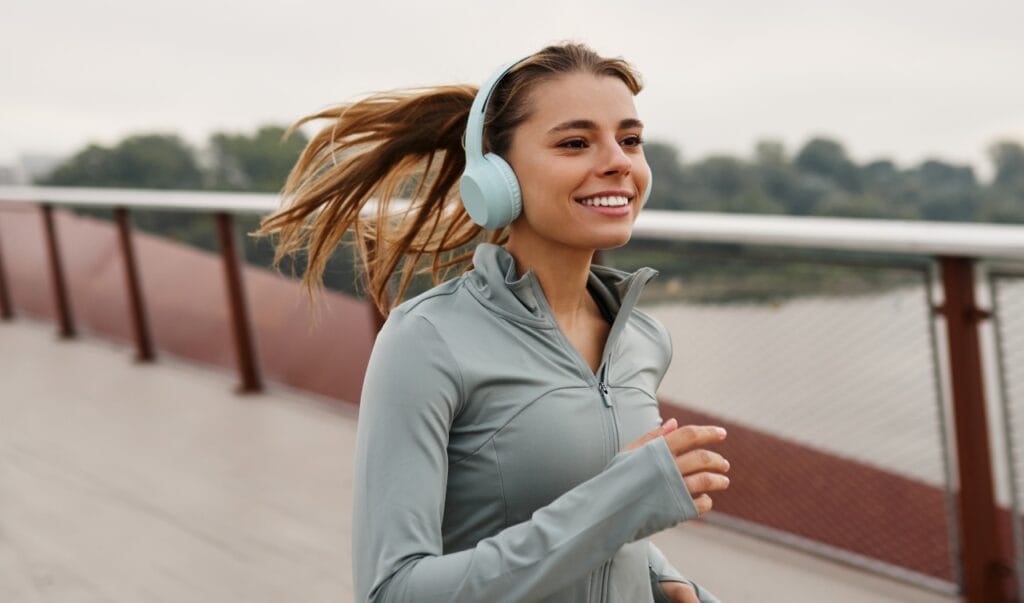 Trucuri pentru autonomie extinsă la căști wireless în timpul alergării femeie alergând pe pod purtând căști wireless over ear, autonomie baterie optimizată la antrenament