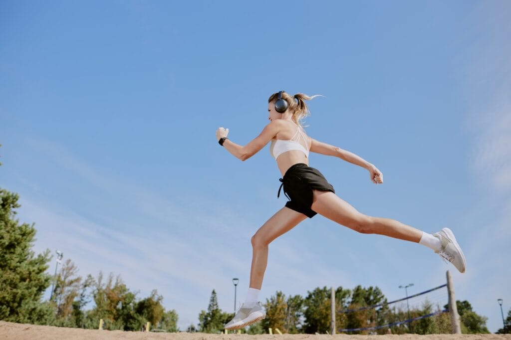 Rezistența căștilor wireless la mișcare intensă și umezeală femeie alergând cu săritură largă, căști wireless over ear, rezistență la praf și umezeală, sport outdoor