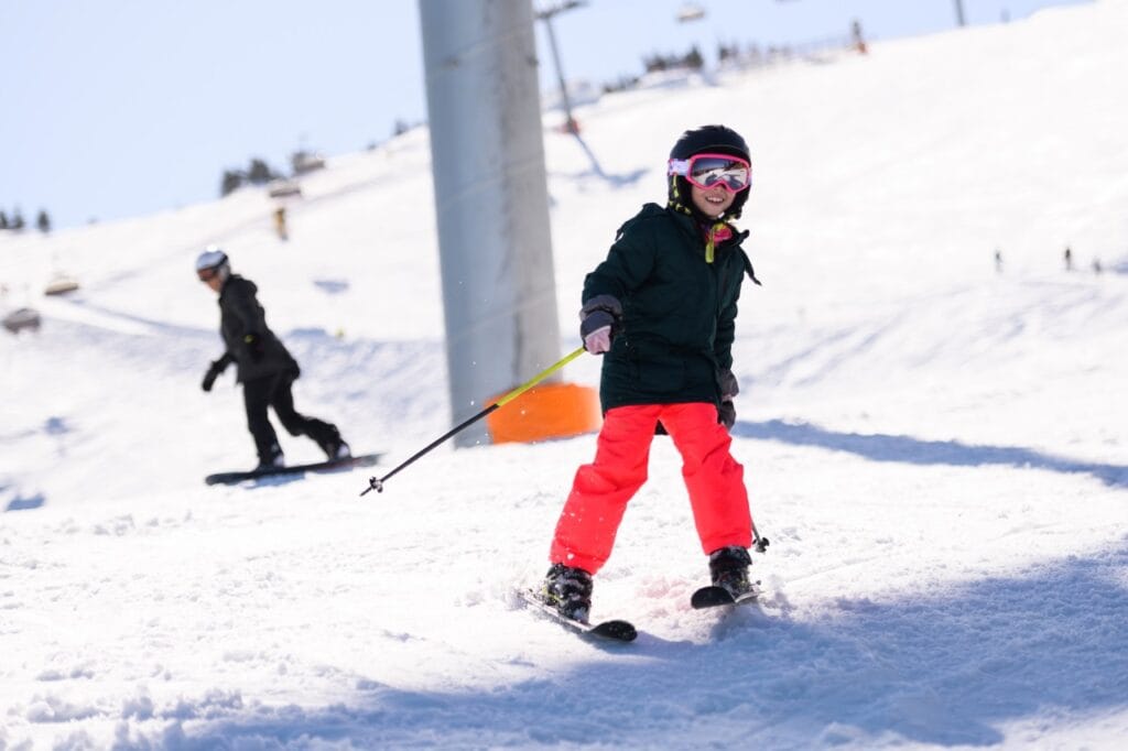 Copil pe pârtie cu pantaloni de schi impermeabili, protejat de umezeală în timpul schiului
