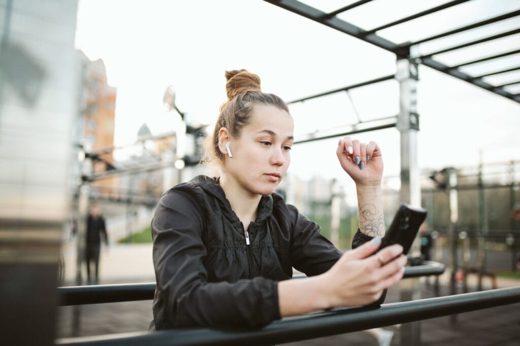 Testarea latenței audio la căști wireless în timpul antrenamentelor cu playlisturi dinamice femeie testează căști wireless pentru latență audio înainte de alergare la un antrenament outdoor