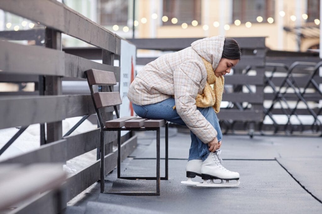 Femeie care își pune patine de gheață pe bancă, detaliu pe modul corect de întreținere pentru rezistență sporită