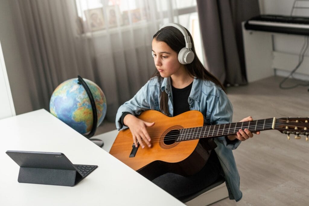 adolescentă învață la chitară acustică la birou, lecții online, alegere dimensiune instrument