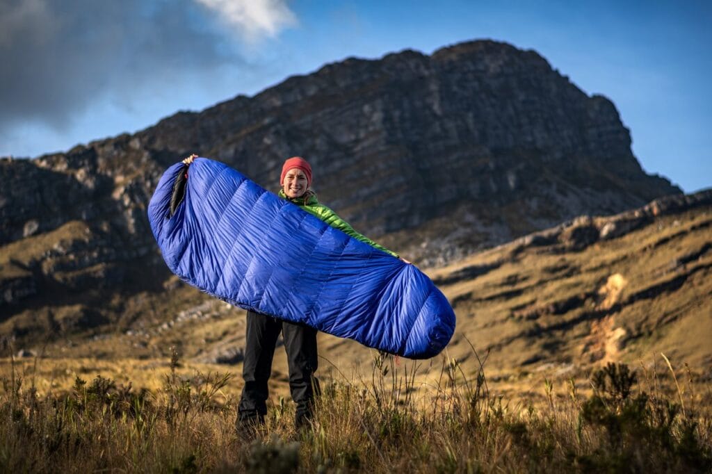 Excursionist arătând un sac de dormit lung tip mumie, cu peisaj montan, evidențiază alegerea corectă a sacului de dormit pentru persoane înalte