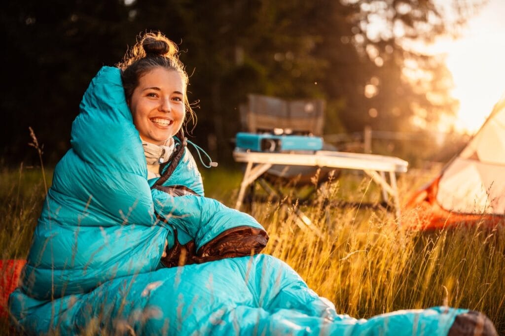 Imagine camping cu femeie în sac de dormit turcoaz, evidențiind confortul tehnologiilor noi pentru sacii de dormit de top
